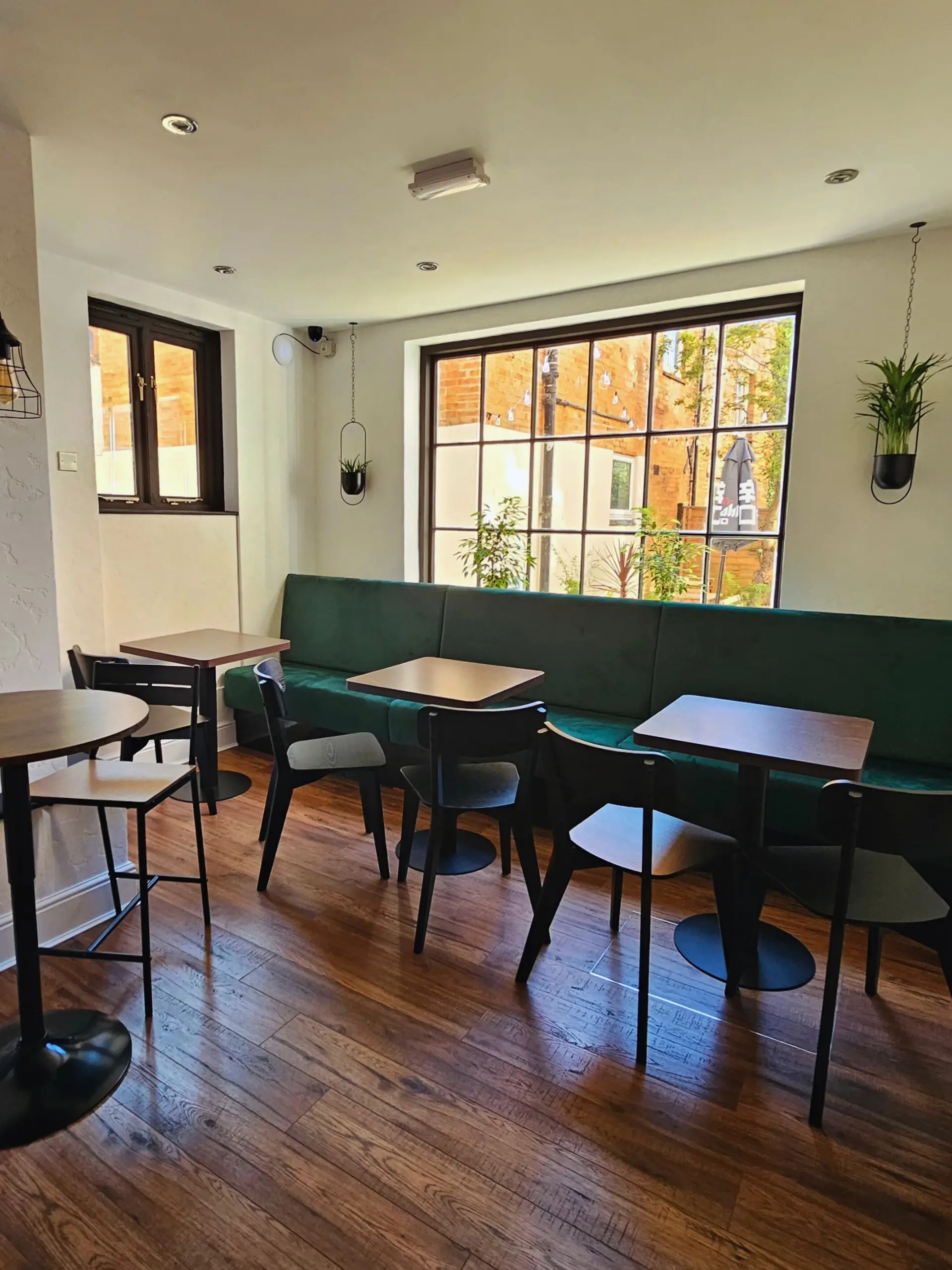Interior of The Wine Shed featuring green velvet bench seating, wooden floors, black chairs, and large windows with natural light